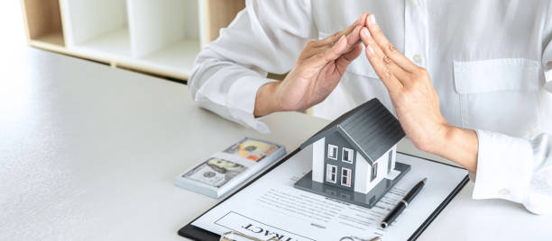Insurance and care protection of house concept, businessman estate agent with protective gesture of small home model by hands.