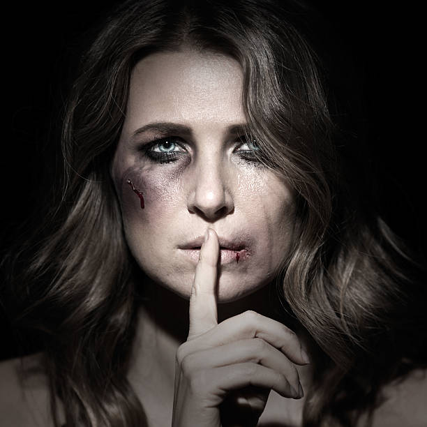 Portrait of abused woman with bruises holding her finger over mouth.