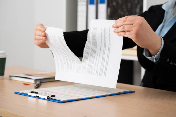 Close-up of the hands of a businesswoman tearing up the signed contract document sitting at a desk in the office